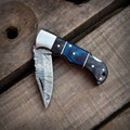 Handmade Damascus steel folding pocket knife with blue wood handle and leather sheath